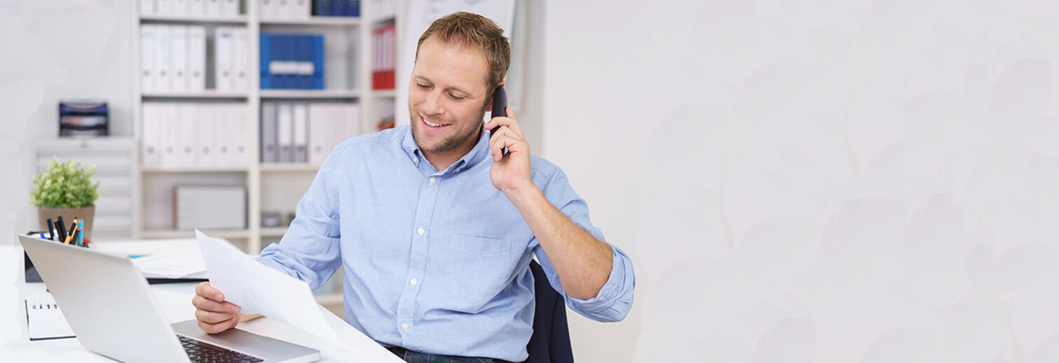 Mann telefoniert im Büro und schaut auf Unterlagen