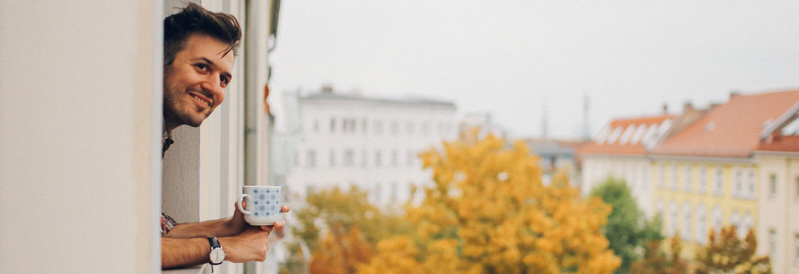 Mann mit Kaffeetasse genießt die Aussicht aus seinem Fenster.